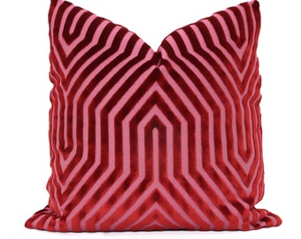 May include: A decorative throw pillow with a geometric pattern. The pillow features a design of alternating red and pink stripes, creating a striking visual effect. The pillow is made of a soft, plush material.
