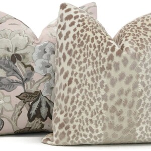 May include: Two decorative throw pillows, one with a pink background and a floral pattern in shades of gray and brown, and the other with a beige background and a brown leopard print.