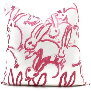 Puede incluir: Almohada blanca con un patr&oacute;n de conejos rosas. Los conejos est&aacute;n dibujados de una manera simple y estilizada.