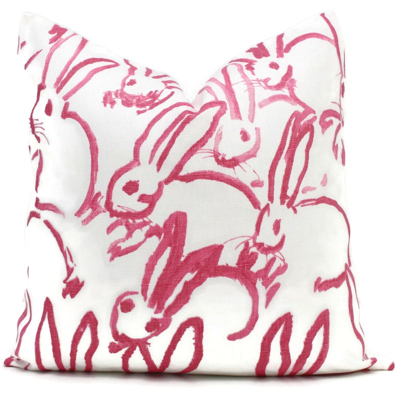 Puede incluir: Almohada blanca con un patr&oacute;n de conejos rosas. Los conejos est&aacute;n dibujados de una manera simple y estilizada.