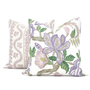 May include: Two decorative throw pillows with floral patterns. One pillow features a white background with purple and pink flowers and green leaves. The other pillow has a white background with a pink and purple paisley pattern.