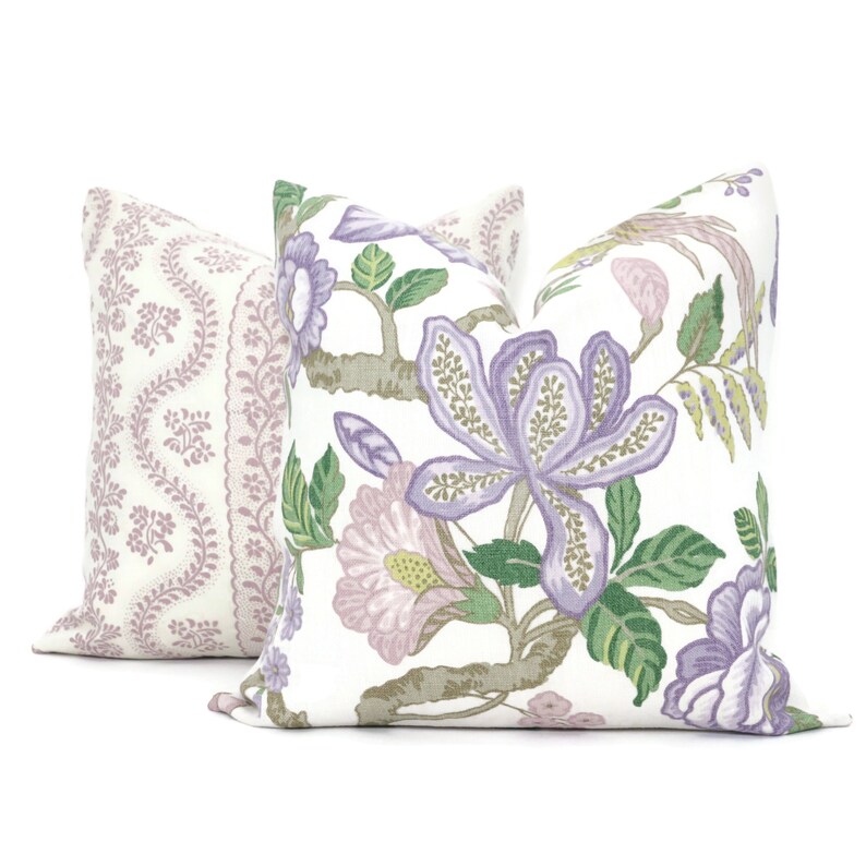May include: Two decorative throw pillows with floral patterns. One pillow features a white background with purple and pink flowers and green leaves. The other pillow has a white background with a pink and purple paisley pattern.