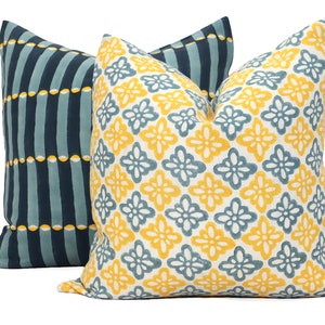 May include: Two decorative throw pillows with a geometric pattern. One pillow is blue and white with vertical stripes and yellow circles. The other pillow is white with a yellow and blue floral pattern.