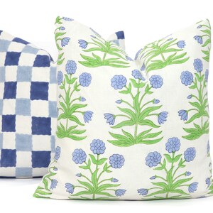 Puede incluir: Dos almohadas decorativas, una con un patr&oacute;n a cuadros azul y blanco y la otra con un fondo blanco y un patr&oacute;n floral con flores azules y hojas verdes.