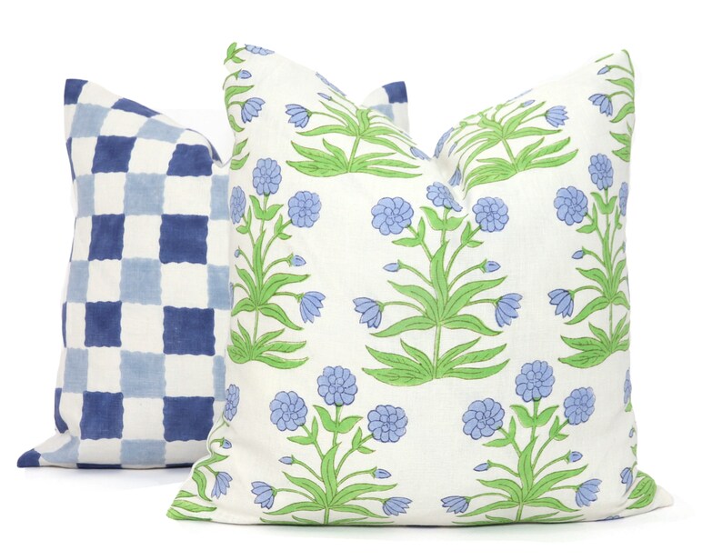 Puede incluir: Dos almohadas decorativas, una con un patr&oacute;n a cuadros azul y blanco y la otra con un fondo blanco y un patr&oacute;n floral con flores azules y hojas verdes.