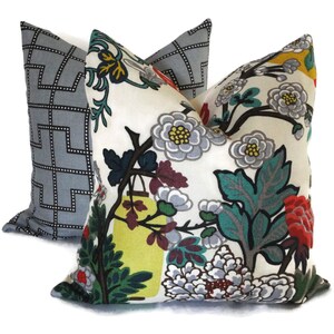 May include: Two decorative throw pillows. One is light gray with a black geometric pattern. The other pillow has a white background with a colorful floral design featuring gray, red, yellow, and teal accents.