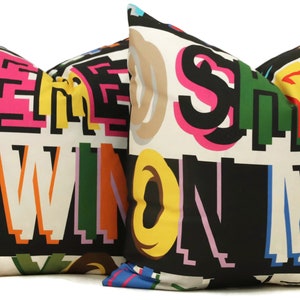 Può includere: Due cuscini da lancio neri e bianchi con una stampa grafica colorata delle parole "Free" e "Win on my" in una varietà di caratteri e colori.