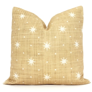 May include: A decorative throw pillow with a tan linen-like fabric. The pillow features a repeating pattern of white starbursts and small white dots. The pillow is square and has a soft, inviting appearance.