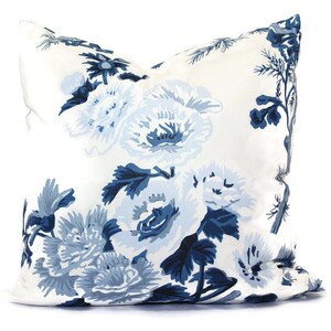 May include: A square decorative pillow with a white background and a large floral pattern in shades of blue. The flowers are stylized and cover the entire surface of the pillow, creating a classic and elegant look.