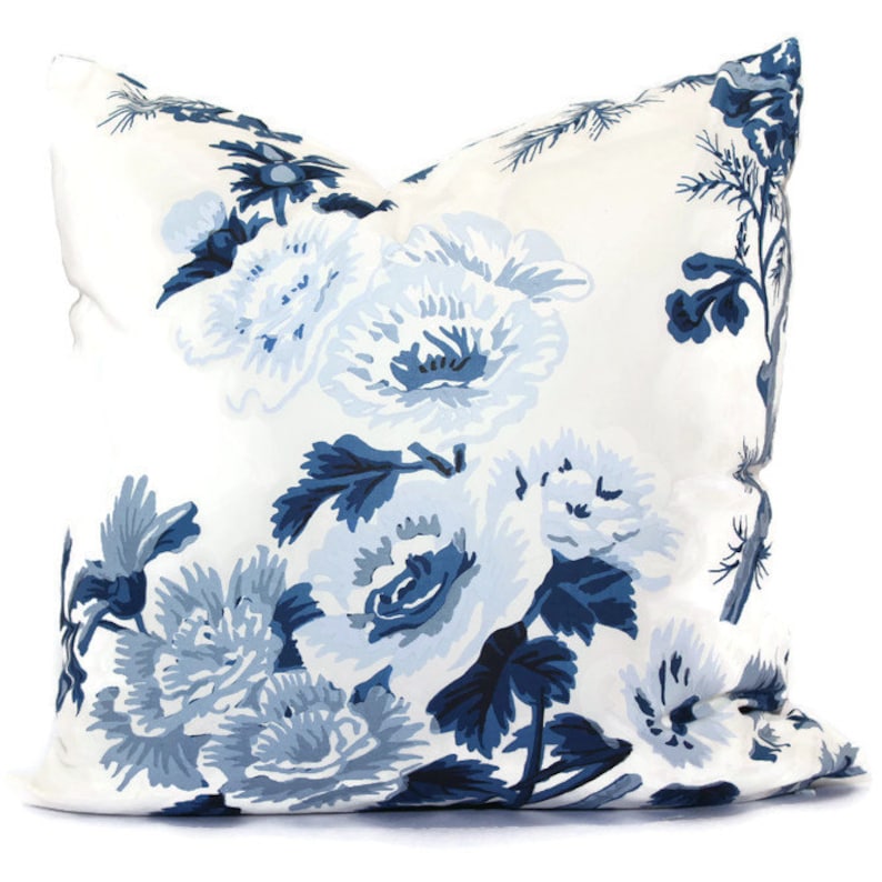 May include: A square decorative pillow with a white background and a large floral pattern in shades of blue. The flowers are stylized and cover the entire surface of the pillow, creating a classic and elegant look.