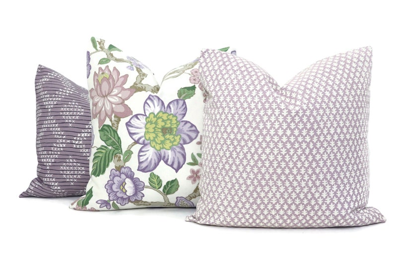 May include: Three decorative throw pillows with floral and geometric patterns. The pillows are in shades of purple, white and green.