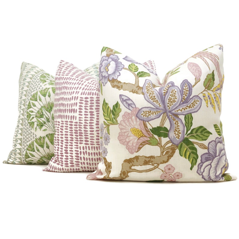 May include: Three decorative throw pillows with floral patterns. The pillow on the left has a green and white floral pattern. The middle pillow has a pink and white geometric pattern. The pillow on the right has a white background with a pink and purple floral pattern.