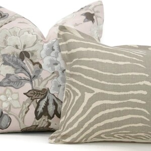May include: Two decorative throw pillows, one with a pink background and a floral pattern in shades of gray, brown, and white, and the other with a beige background and a zebra stripe pattern.