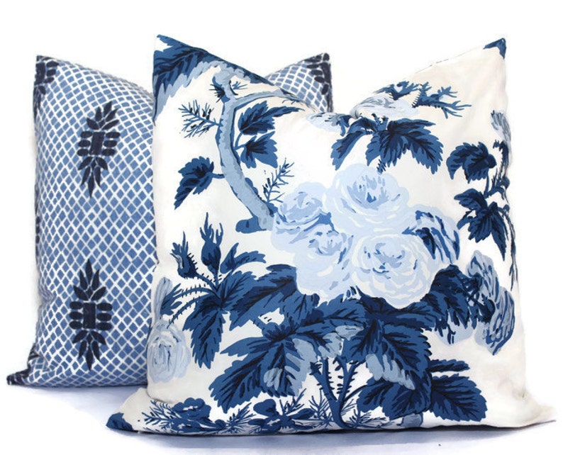 May include: Two decorative throw pillows. One pillow features a blue and white floral pattern with roses and foliage. The other pillow has a blue and white geometric trellis design with a floral motif.