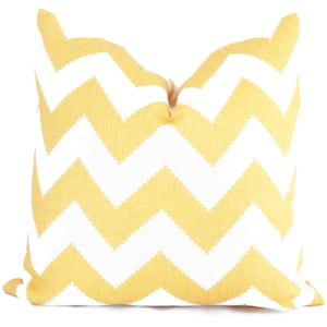 Puede incluir: Cojín cuadrado con un patrón de chevrón amarillo y blanco. El cojín tiene un aspecto suave y texturizado y está relleno de un material esponjoso. El diseño en zigzag añade un toque moderno a la decoración del hogar.