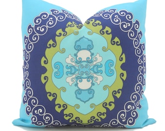 May include: A square cushion with a striking, symmetrical pattern. The design features a light blue background with a central pattern in shades of blue, green, and white. The pattern includes swirling, scroll-like elements.