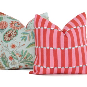 May include: Two decorative throw pillows, one with a light blue background and a floral pattern in shades of pink, green, and brown, and the other with a pink background and a striped pattern with white and blue accents.