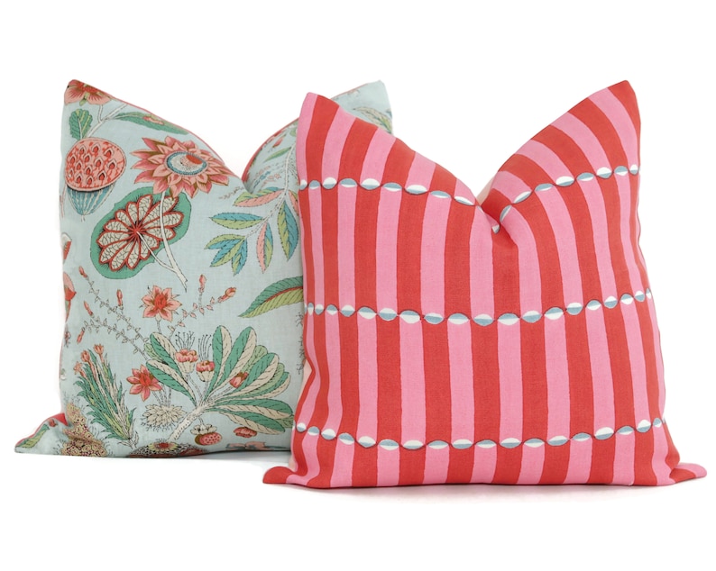 May include: Two decorative throw pillows, one with a light blue background and a floral pattern in shades of pink, green, and brown, and the other with a pink background and a striped pattern with white and blue accents.