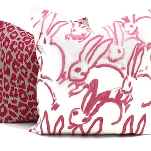 Puede incluir: Dos almohadas decorativas. Una almohada es rosa y blanca con un patr&oacute;n de conejos rosas. La otra almohada es rosa y beige con estampado de leopardo.