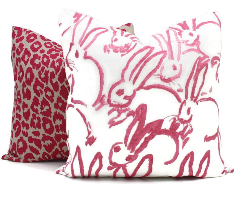 Puede incluir: Dos almohadas decorativas. Una almohada es rosa y blanca con un patr&oacute;n de conejos rosas. La otra almohada es rosa y beige con estampado de leopardo.