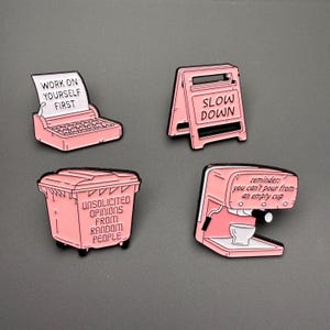 Puede incluir: Cuatro pines de esmalte rosa con contornos negros. Los pines presentan una máquina de escribir con el texto "WORK ON YOURSELF FIRST", un letrero de "SLOW DOWN", un cubo de basura con "UNSOLICITED OPINIONS FROM RANDOM PEOPLE", y una máquina de espresso con "you can't pour from an empty cup".