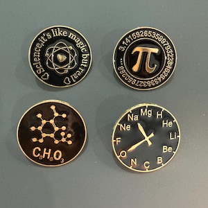 May include: Four circular enamel pins with black backgrounds and gold-colored metal accents. One features an atom with a heart and the text Science, it's like magic but real. Another displays the pi symbol with digits. One shows a chemical structure with C8H8O3, and the last is a clock face with chemical element symbols.