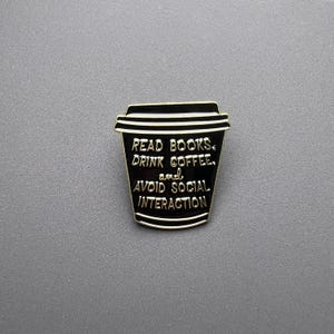 Könnte beinhalten: Eine weiße Keramik-Tasse mit schwarzem Henkel und dem Text "But First, Coffee" in schwarzer, handschriftlicher Schrift. Die Tasse steht auf einer weißen Oberfläche.