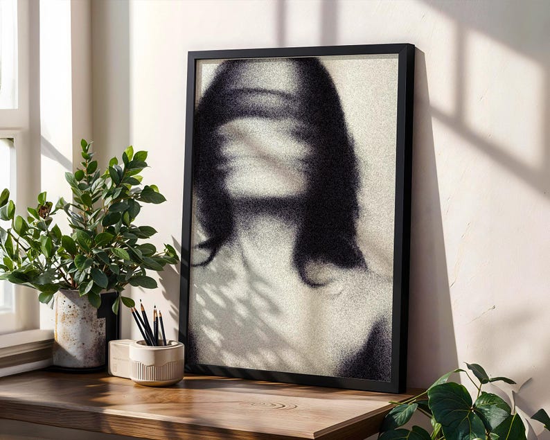 Puede incluir: Una impresi&oacute;n art&iacute;stica en blanco y negro enmarcada que presenta una imagen borrosa de una persona. La obra de arte se exhibe sobre una superficie de madera, junto a una planta en maceta y un portal&aacute;pices con l&aacute;pices.