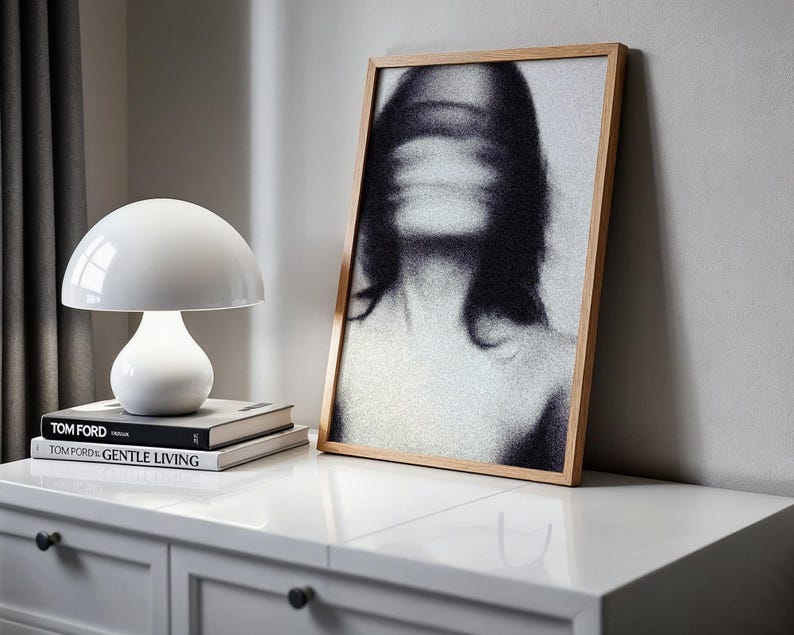 Puede incluir: Una l&aacute;mpara de mesa blanca con forma de hongo se encuentra sobre una pila de libros con los t&iacute;tulos "TOM FORD" y "TOM FORD GENTLE LIVING". Un retrato en blanco y negro enmarcado con un rostro borroso se apoya contra una pared. La escena est&aacute; ambientada en una c&oacute;moda blanca.