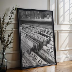 May include: A black and white framed print depicting a collection of vinyl records in a store bin. The labels visible include Rock & Pop H, Jimi Hendrix, and Led Zeppelin. The artwork is encased in a simple black frame and rests on a wooden floor.