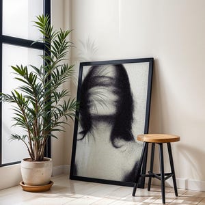 Puede incluir: Una impresi&oacute;n art&iacute;stica enmarcada en negro con un retrato en blanco y negro de una mujer con rasgos faciales borrosos. Un peque&ntilde;o taburete de madera con patas negras est&aacute; cerca. Una planta en maceta con hojas verdes est&aacute; frente a una ventana.