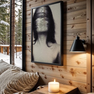 Puede incluir: Un cuadro en blanco y negro con un retrato borroso cuelga de una pared de madera. Una l&aacute;mpara de pared negra y una vela encendida tambi&eacute;n son visibles. La escena est&aacute; ambientada cerca de una ventana con vistas a un bosque nevado.