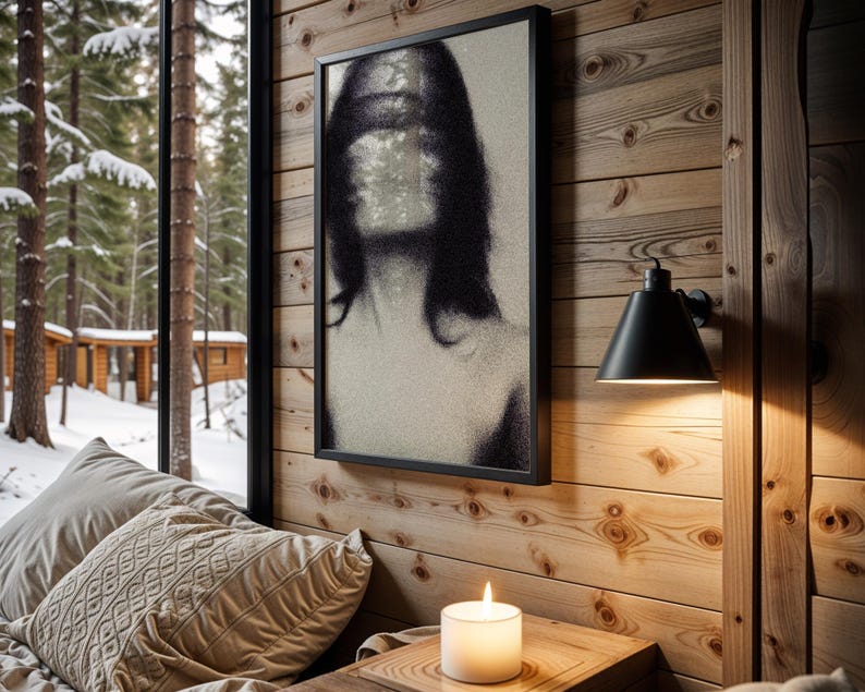 Puede incluir: Un cuadro en blanco y negro con un retrato borroso cuelga de una pared de madera. Una l&aacute;mpara de pared negra y una vela encendida tambi&eacute;n son visibles. La escena est&aacute; ambientada cerca de una ventana con vistas a un bosque nevado.
