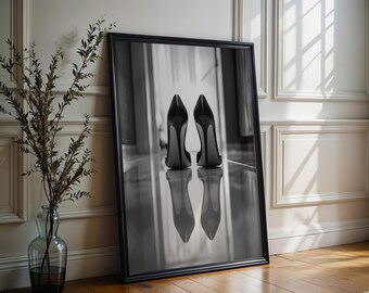 Puede incluir: Una impresión artística enmarcada en blanco y negro que muestra un par de zapatos de tacón alto vistos desde atrás. Los zapatos están colocados sobre una superficie reflectante, creando una imagen especular clara debajo. El marco es fino, negro y rectangular.