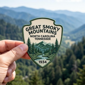 K&ouml;nnte beinhalten: Ein schildf&ouml;rmiger, bestickter Aufn&auml;her mit einer Landschaft aus gr&uuml;nen Bergen, Tannen und einem Fluss. Der Text lautet GREAT SMOKY MOUNTAINS, NORTH CAROLINA, TENNESSEE und 1934. Der Aufn&auml;her hat einen cremefarbenen Hintergrund und einen dunkelgr&uuml;nen Rand.