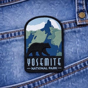 May include: Embroidered patch featuring a black bear silhouette walking in front of a mountain range. The patch has a blue, green, and white color scheme, with the words "YOSEMITE - NATIONAL PARK -" in white text.