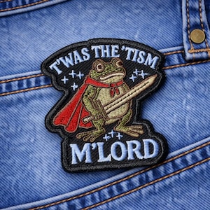 May include: Embroidered patch featuring a frog in a red cape and holding a sword. The patch has the text "T'WAS THE 'TISM M'LORD" in white and blue lettering. The patch is on a blue denim background.