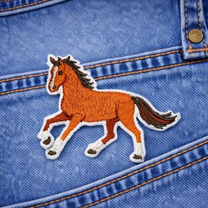 May include: Embroidered patch of a brown horse with a white outline, running across a blue denim background. The horse has a black mane and tail, and white markings on its legs. The denim has visible stitching and a button.
