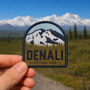 May include: Embroidered patch featuring a mountain landscape with the text "DENALI NATIONAL PARK." The patch has a navy blue border, a light blue sky, and a forest green base. The mountains are white and navy blue.