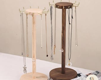 May include: Two wooden jewelry stands with circular bases and vertical poles. Each stand features a round top with multiple gold-toned metal hooks extending outward for hanging necklaces. One stand is light-colored wood, and the other is dark wood.
