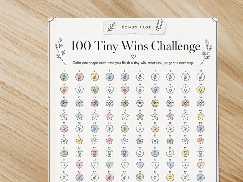 May include: A printable "100 Tiny Wins Challenge" sheet. The sheet features a grid of 100 shapes, including hearts, flowers, and stars, each with a number. The text "100 Tiny Wins Challenge" is at the top, with instructions below.