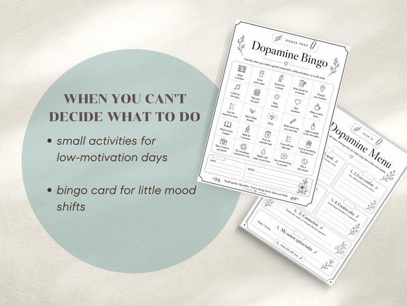 May include: Two white paper sheets with the text "Dopamine Bingo" and "Dopamine Menu" are displayed. The bingo card features a grid of small activities, while the menu lists options for mood shifts. The background is a light green circle with text.