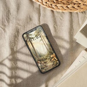 Lifestyle mockup of an Enchanted Forest cottagecore phone theme on a smartphone, featuring botanical woodland wallpaper with trees, mushrooms, and warm neutral styling.