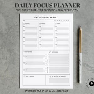 May include: A white Daily Focus Planner with the text "Daily Focus Planner" and "Focus Checklist • Time Blocking • Task Breakdown." A gold and white pencil rests on the right side. The planner includes sections for time blocking, tasks, and notes.