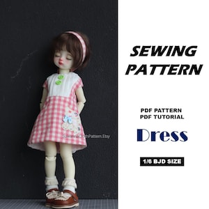 May include: A 1/6 BJD size doll wearing a pink and white gingham dress with a white bodice, two green buttons, and a cat applique. The text reads SEWING PATTERN, PDF PATTERN, PDF TUTORIAL, Dress, 1/6 BJD SIZE, and SuwannaClothPattern.Etsy.