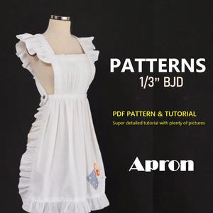 Puede incluir: Un delantal blanco con bordes y correas con volantes, exhibido en un maniquí. El delantal presenta un pequeño parche decorativo y está etiquetado como "PATTERNS 1/3" BJD" con texto que indica un patrón y tutorial en PDF.