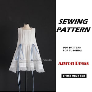 May include: A white sleeveless apron dress featuring vertical pleats, lace trim at the hem, and long light blue ribbons tied at the waist. The text SEWING PATTERN, PDF PATTERN, PDF TUTORIAL, Apron Dress, and Blythe OB24 Size are displayed on the right.
