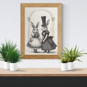 May include: A framed grayscale print featuring two anthropomorphic rabbits in Victorian-era attire. One rabbit wears a top hat and a dark dress, while the other wears a ruffled dress. The artwork is set against an architectural backdrop.