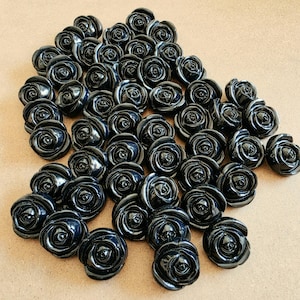 May include: A collection of numerous small, glossy black buttons shaped like blooming roses. Each button features intricate, layered petal details arranged in a circular pattern, creating a uniform appearance across the entire set of individual pieces.