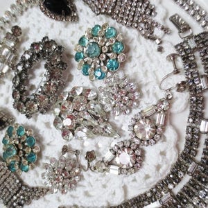 May include: A collection of vintage rhinestone jewelry pieces, including necklaces, earrings, and brooches. The jewelry is made of silver-toned metal and features clear and blue rhinestones.